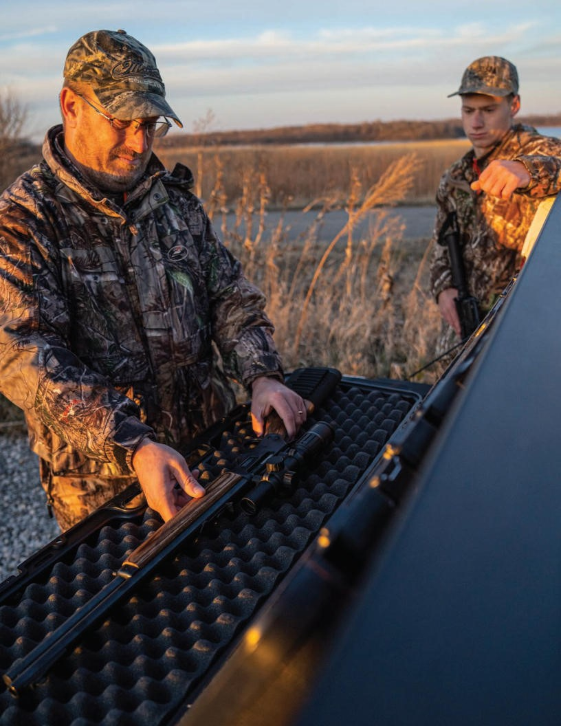 father and son in wetlands hunting area with rifle in gun case with foam insert